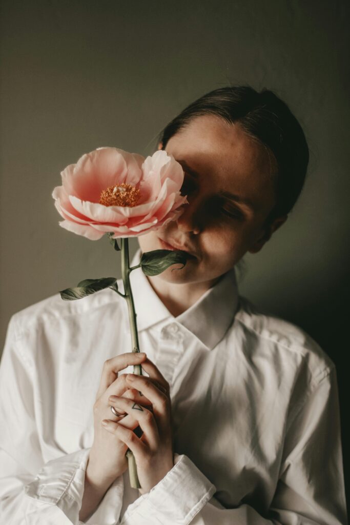 Frauen mit speziellen Anliegen Person hält eine große rosa Blüte vor das Gesicht – Natürlichkeit und Selbstausdruck