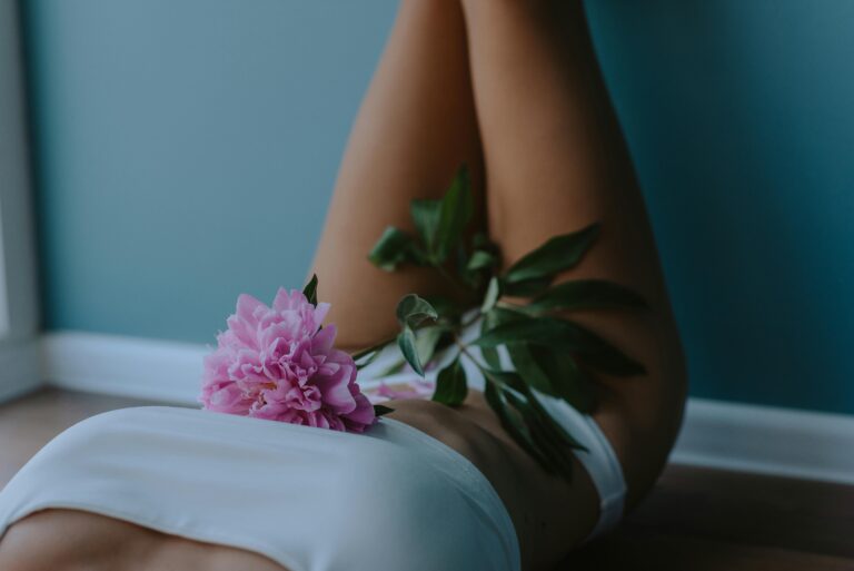 Vorsorge_Kontrolluntersuchung Frau liegt entspannt auf einem Bett, hält eine rosa Blüte – sinnbildlich für Wohlbefinden und Weiblichkeit